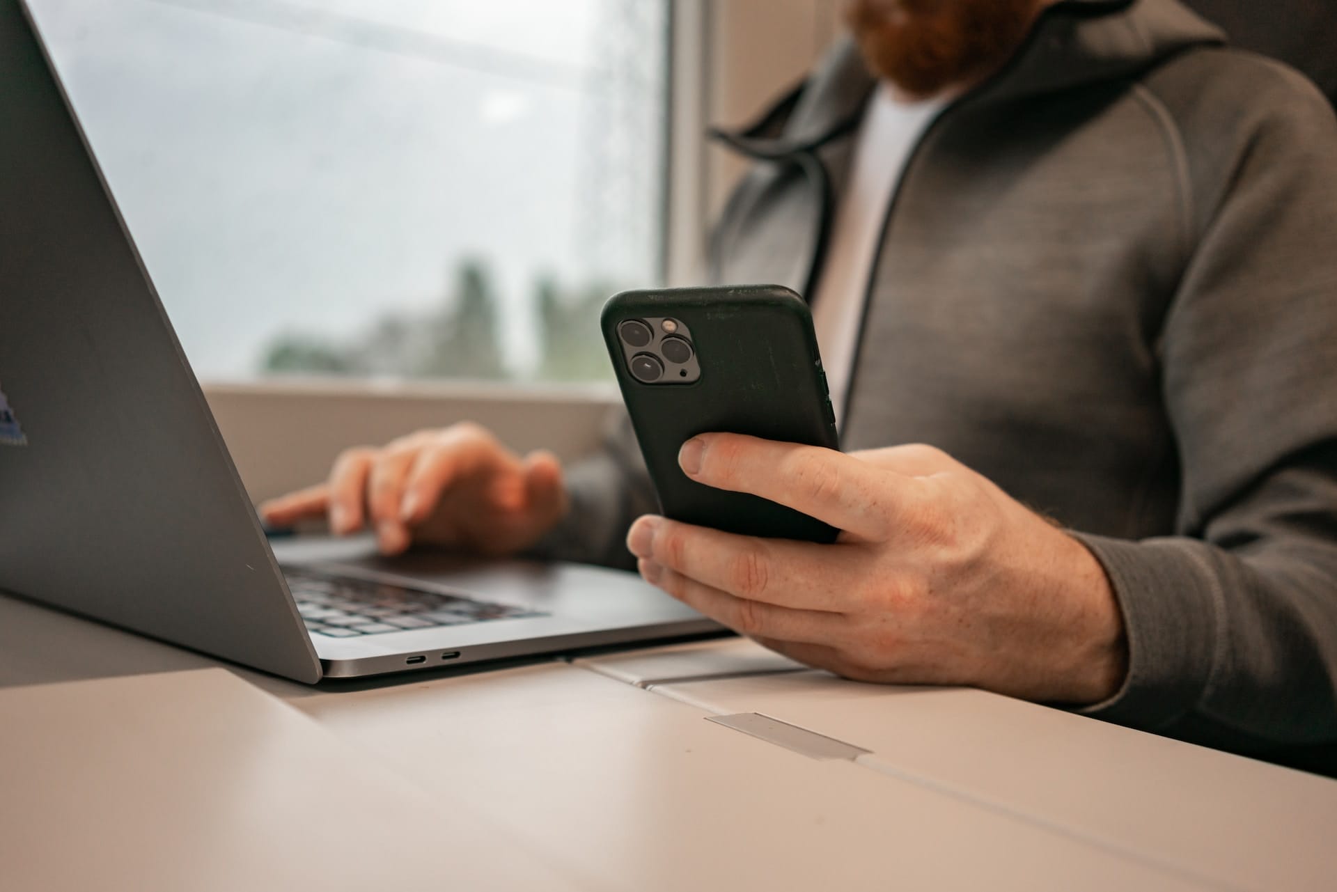 A man using a cell phone while sitting in front of a laptop, working on website development using AWS.