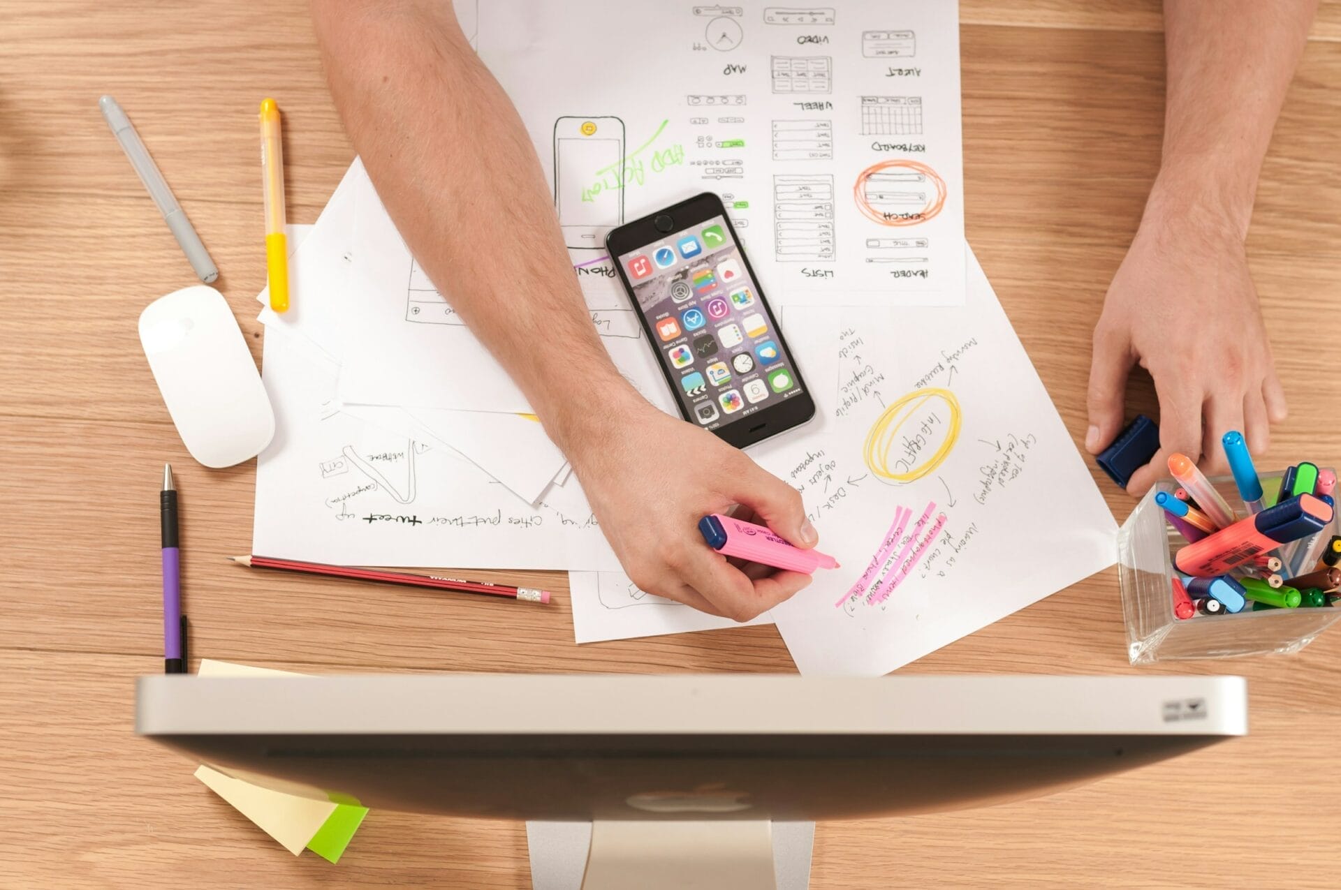 A person working with Sculpted Marketing on a computer with a cell phone and pens. He is learning How Google Ads Help You Advance Your Business Goals